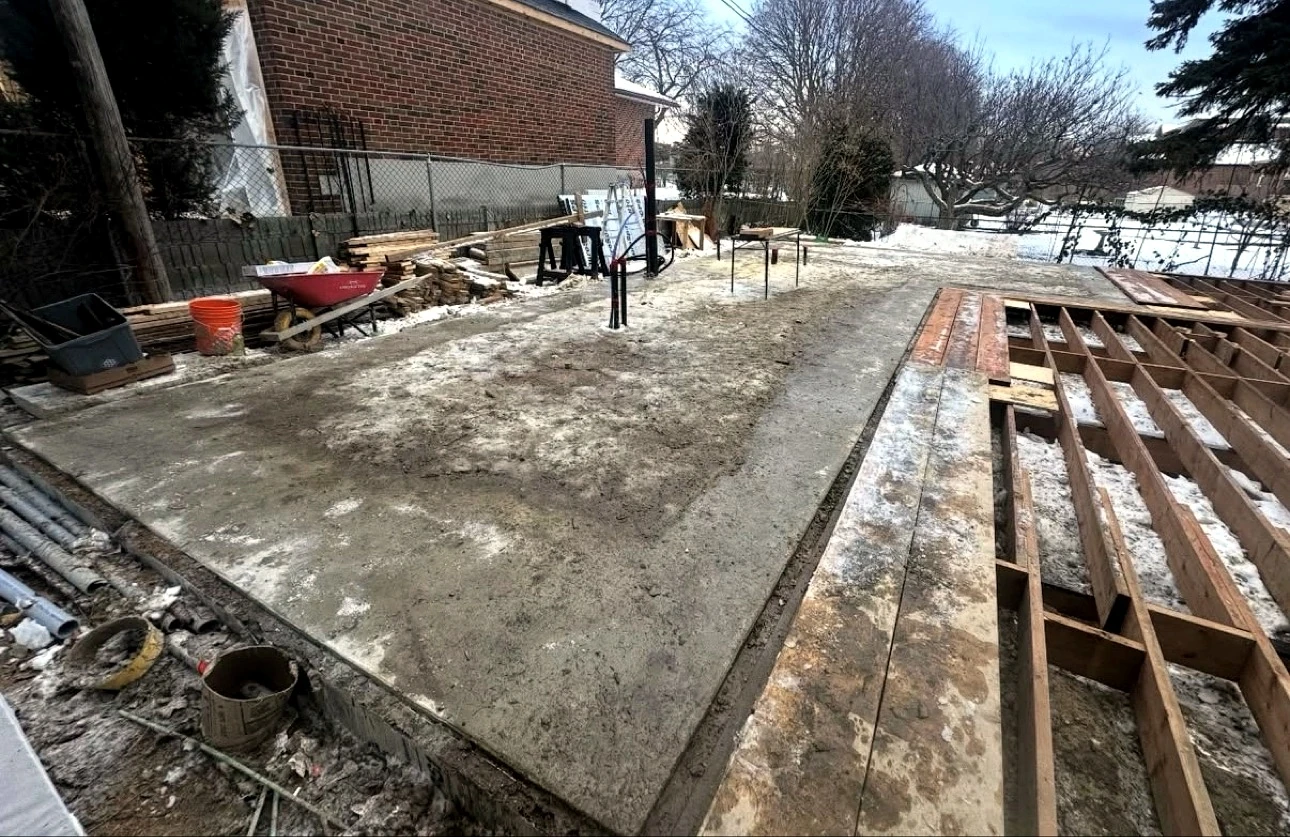Real Pisces jobsite in winter: concrete slab and wood deck framing on the backyard jobsite