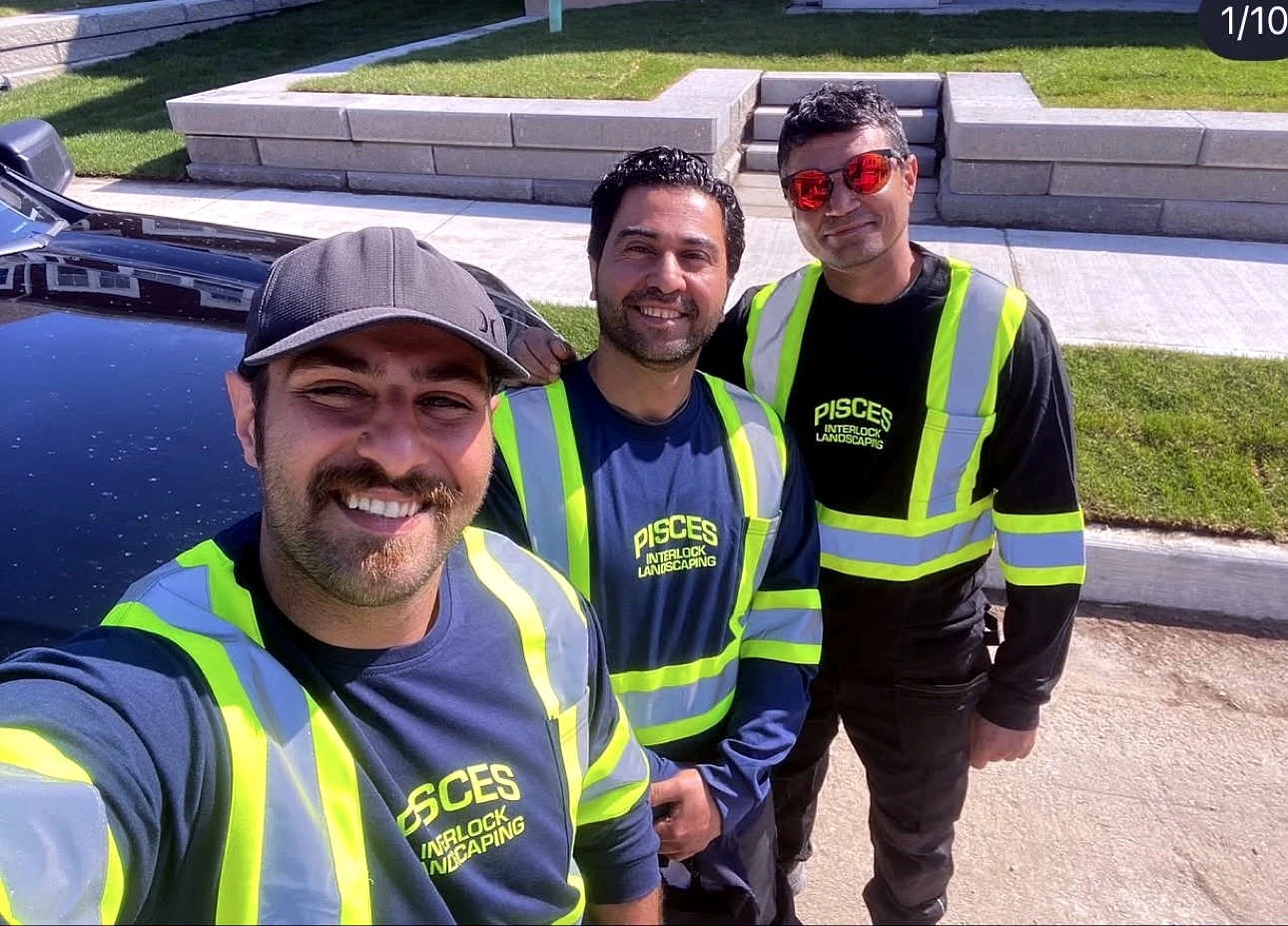 The Pisces crew on a jobsite &mdash; three smiling team members in PISCES INTERLOCK LANDSCAPING shirts and hi-vis vests