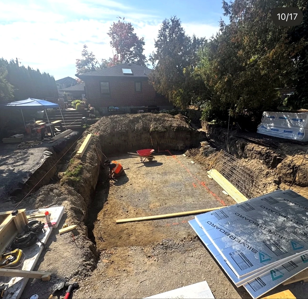 Real Pisces jobsite: excavated foundation pit with a crew member doing layout, wheelbarrow and rebar mesh