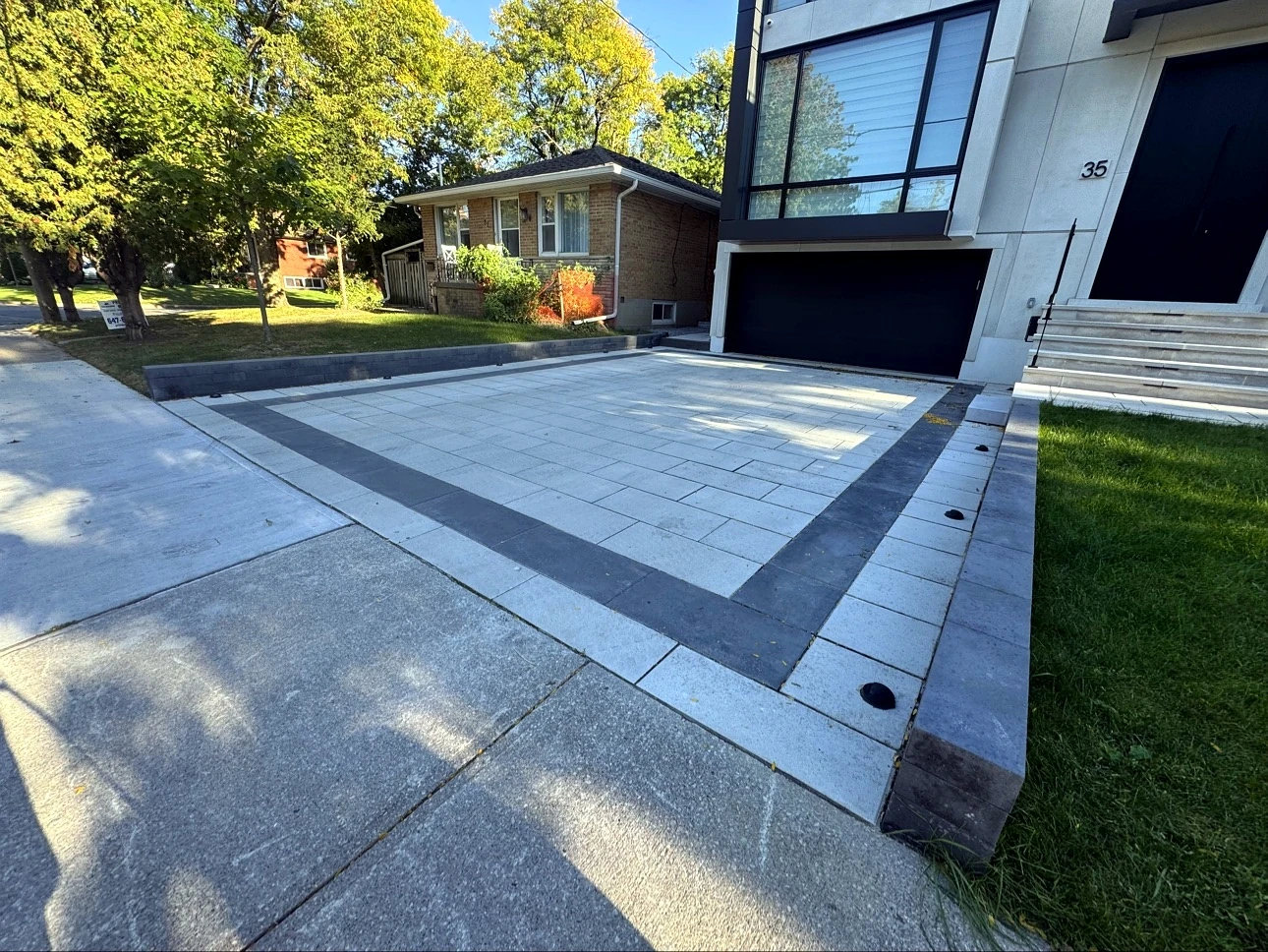 Finished Pisces interlock driveway in Toronto — charcoal border frame, stone retaining wall and lawn